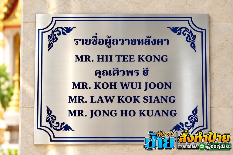 ป้ายสแตนเลสสีเงินผิวปัดลายแนวนอน แสดงรายชื่อผู้ถวายหลังคาวัดด้วยตัวอักษรสีน้ำเงินเข้ม ตกแต่งกรอบเส้นคู่และลวดลายไทยประยุกต์ทั้งสี่มุม ติดตั้งบนผนังหินอ่อน